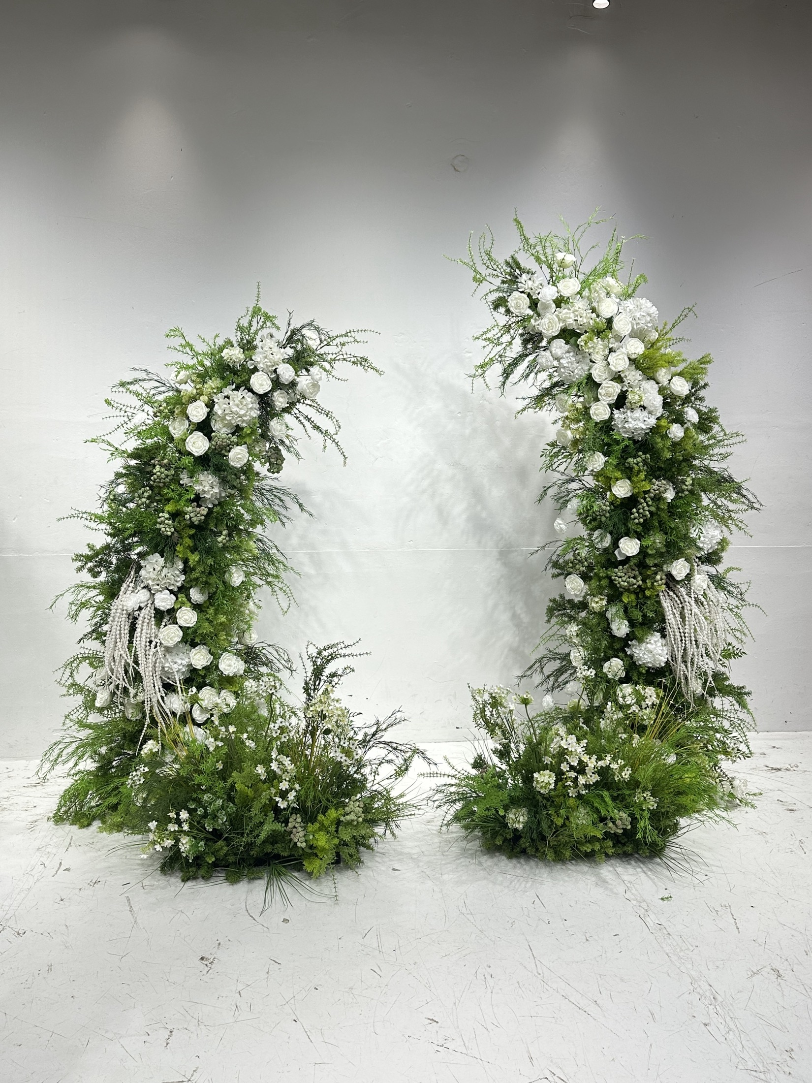 Horn-shaped faux-flower arch with forest greenery, white flowers and ground florals